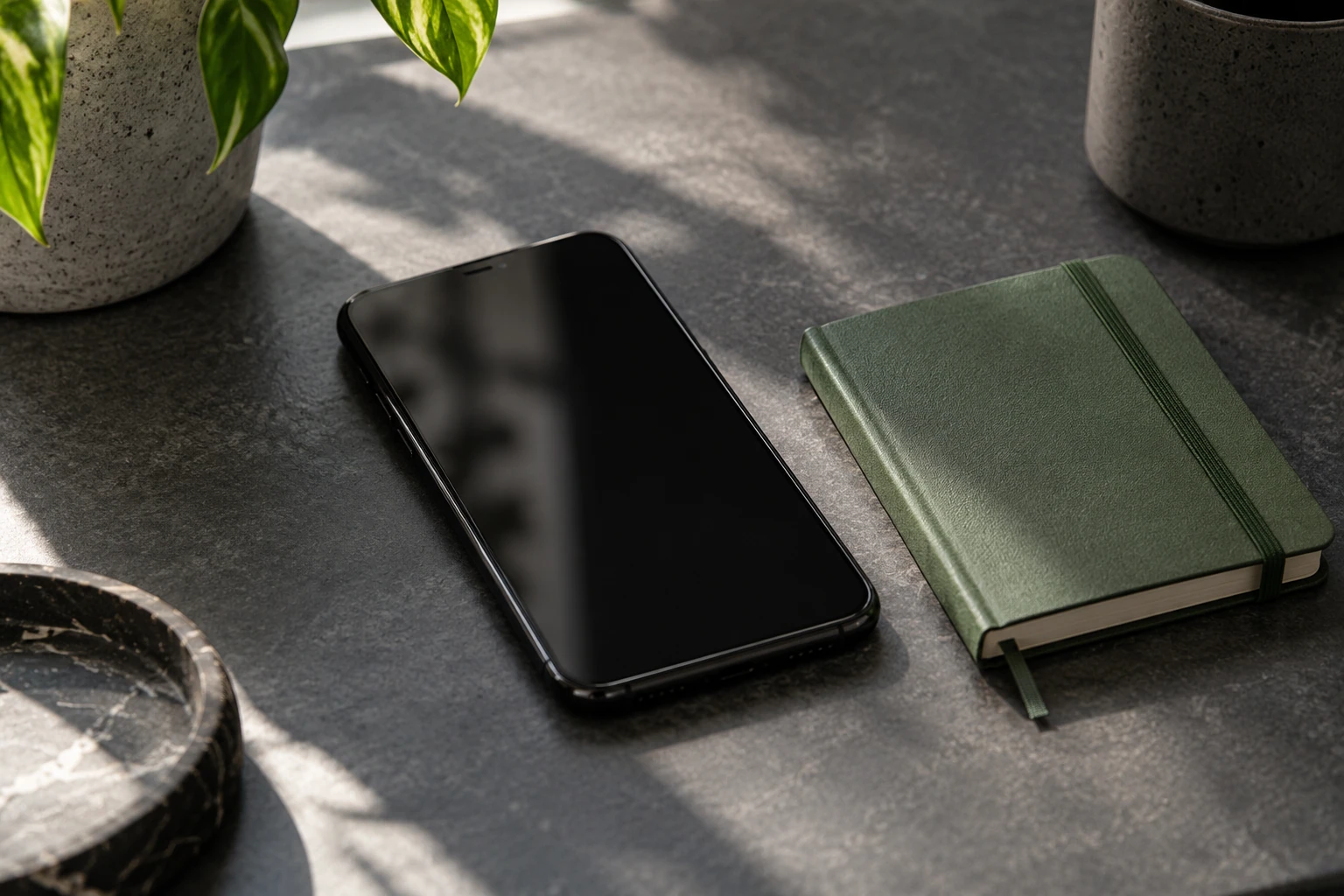 Smartphone éteint posé sur table près d'un carnet vert et plantes en lumière naturelle
